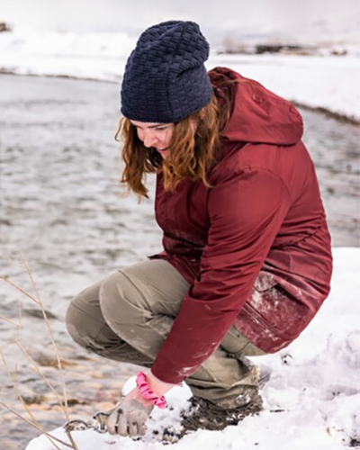 Anna Monson smiling in the snow by the Provo river next to a plant